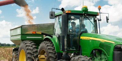 Green tractor harvesting crops in a sunny rural field, showcasing modern agriculture.