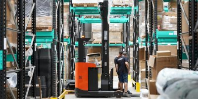 Warehouse scene featuring workers and a forklift navigating aisles for logistics and inventory management.